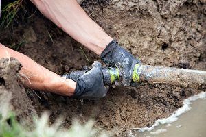 A man is fixing a pipe in the mud.