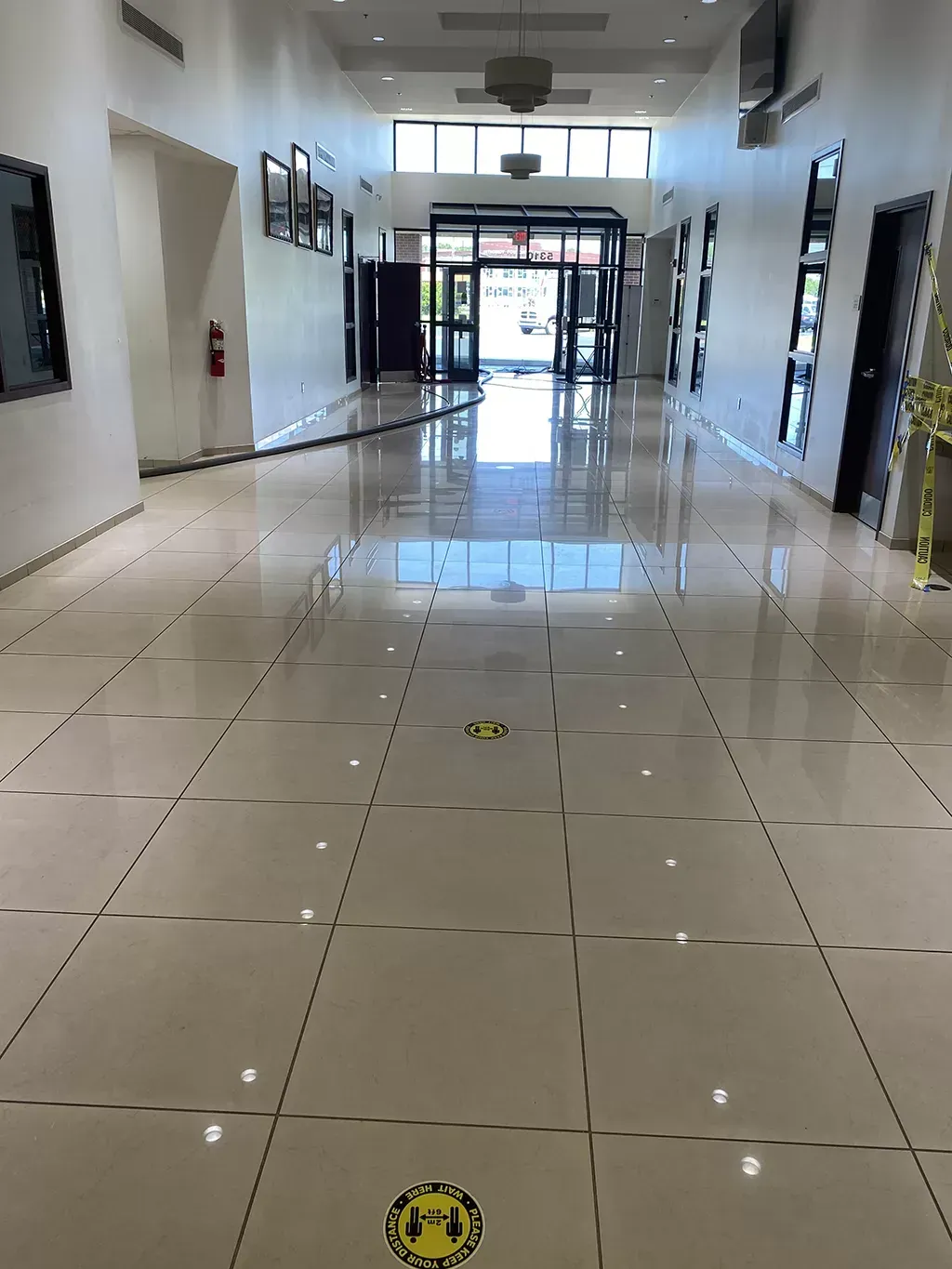 Long hallway with glossy tiled floor, social distancing markers, and an exit with glass doors.