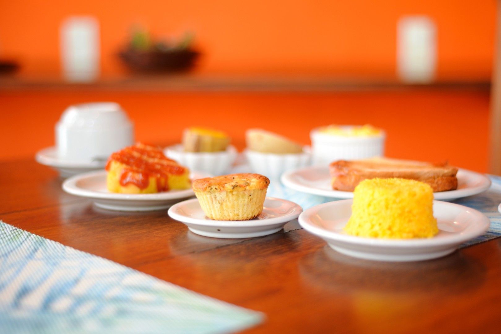 Mini sobremesas variadas em pratos brancos sobre uma mesa de madeira com fundo laranja.