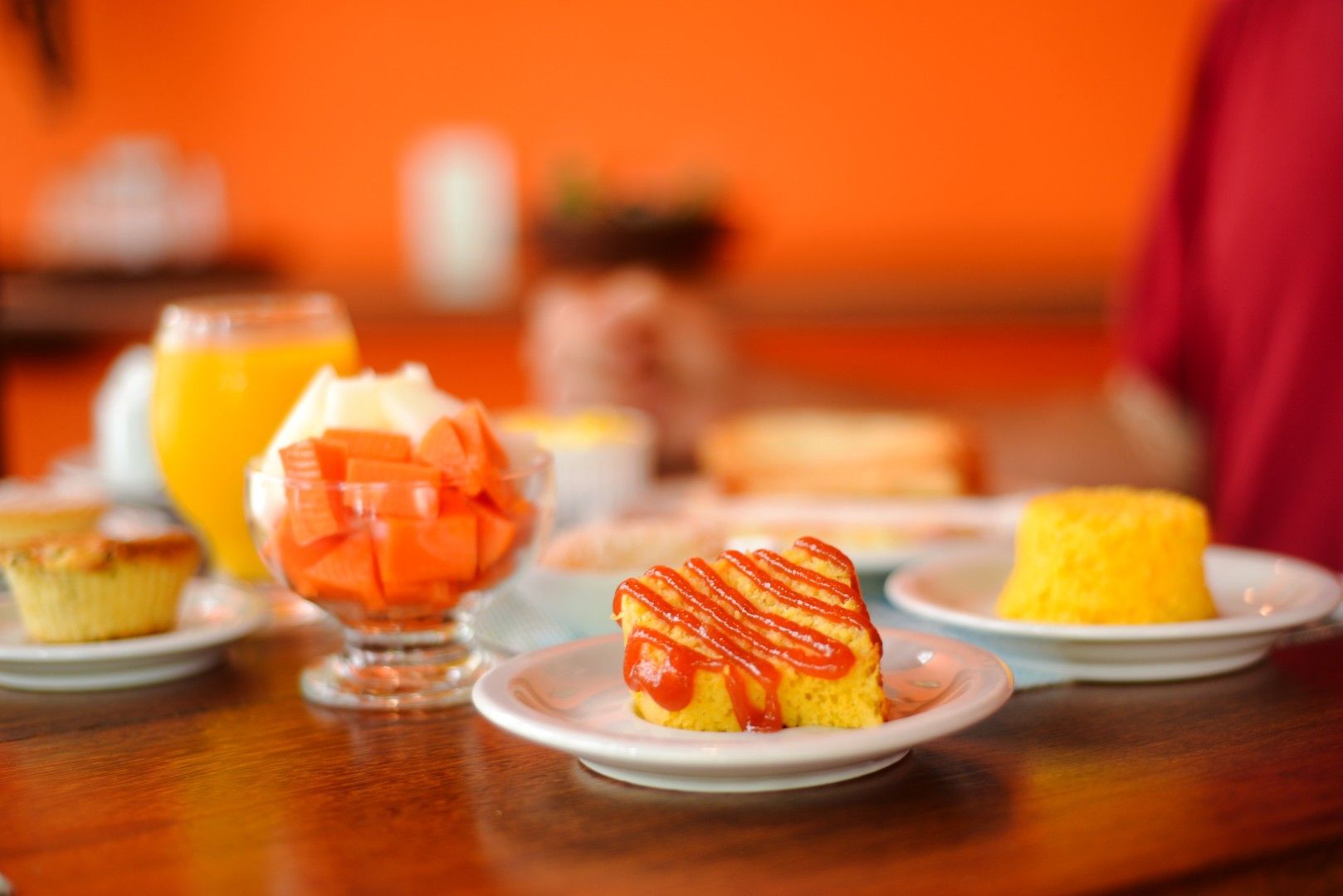 Sobremesas em pratos e copos sobre uma mesa de madeira, incluindo gelatina de laranja e pedaços de bolo com cobertura.
