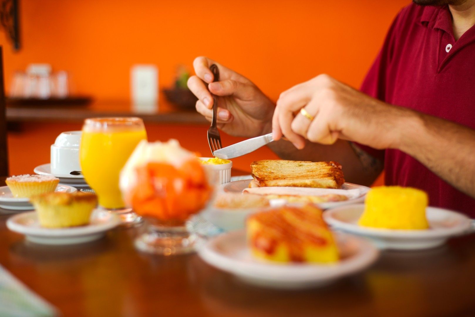 Mãos tomando café da manhã em uma mesa com suco de laranja e doces.