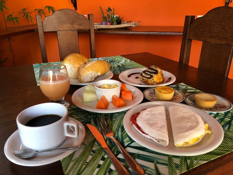 Buffet de café da manhã: mamão fatiado, queijo, doces e uma panela elétrica de cozimento lento sobre uma bancada preta.