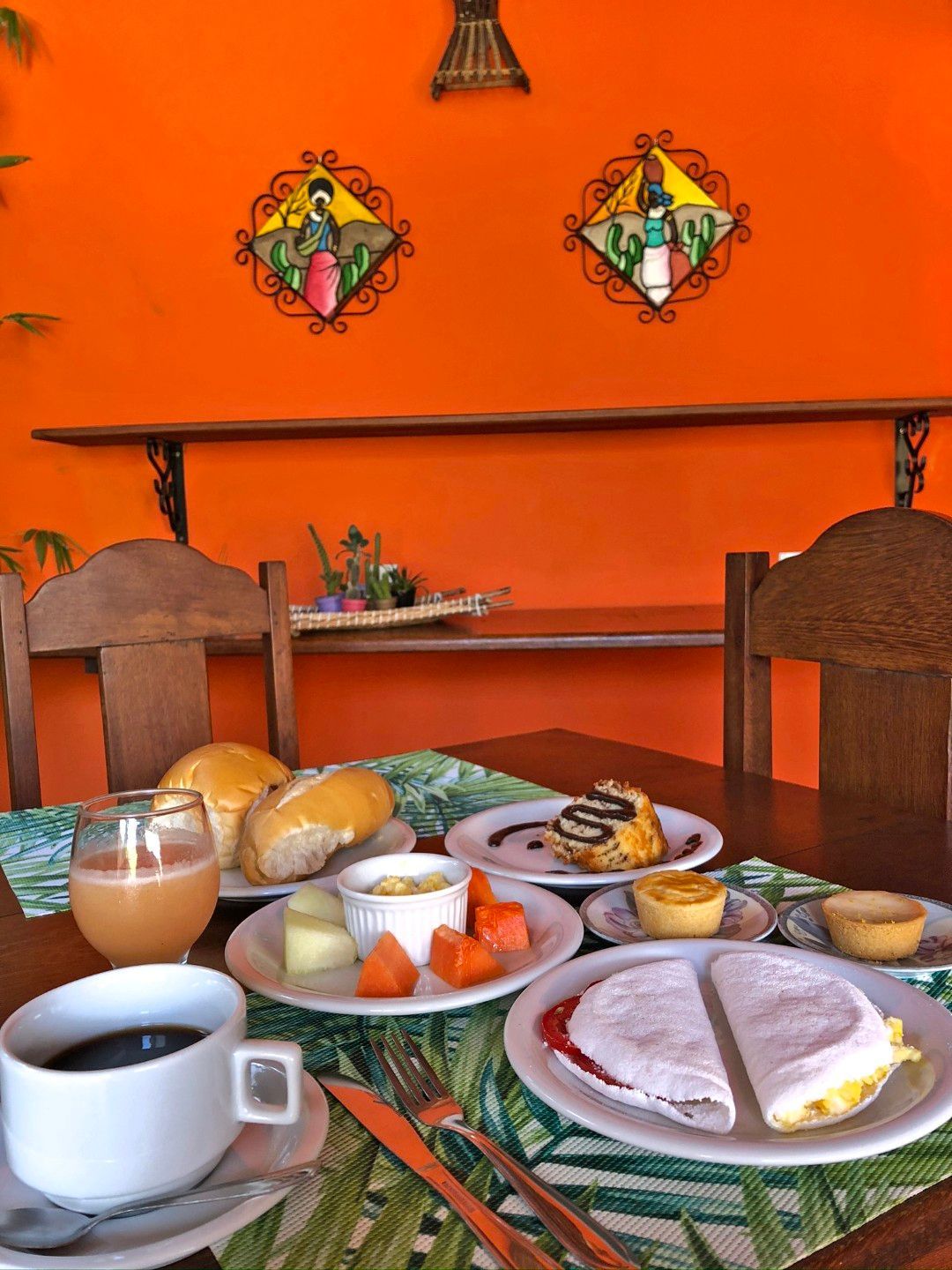 Mesa de café da manhã com café, pão, ovos e frutas em um café laranja vibrante.