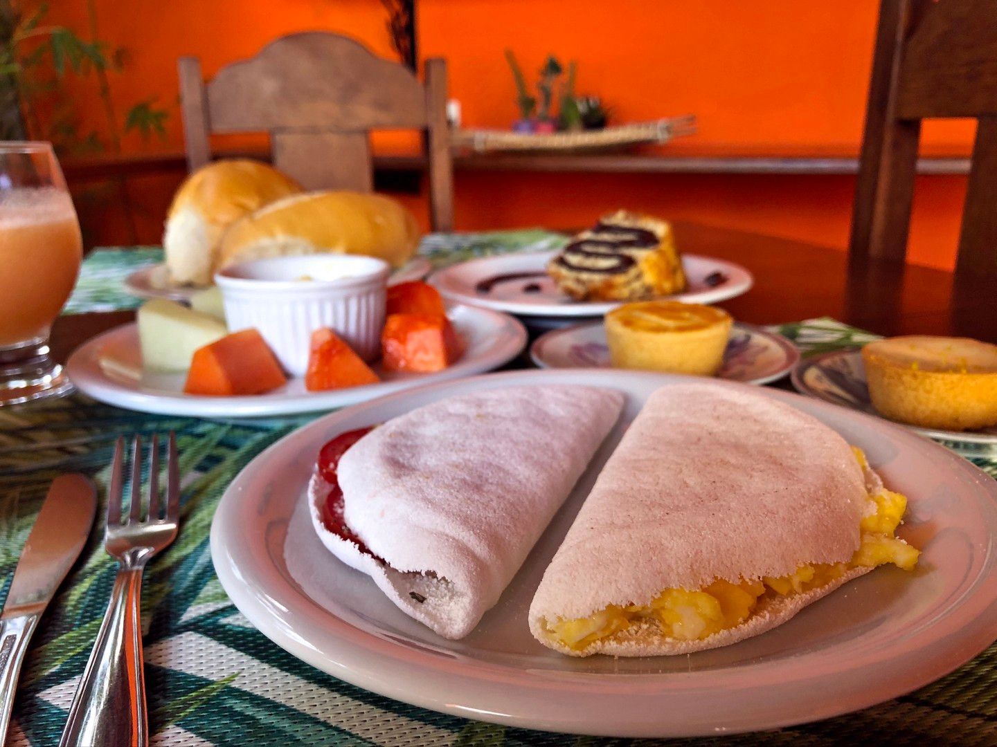 Duas travessas de pastelaria sobre uma mesa com outros pratos de pequeno-almoço e paredes alaranjadas ao fundo.