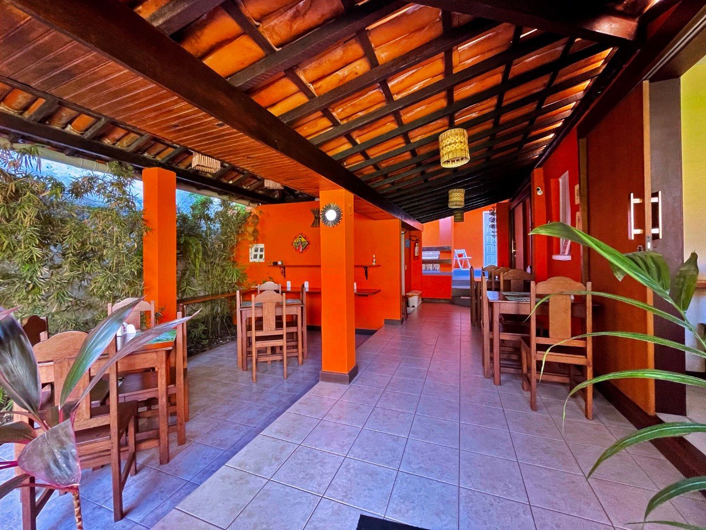 Pátio de restaurante ao ar livre com paredes laranja, mesas de madeira e teto de telhas.