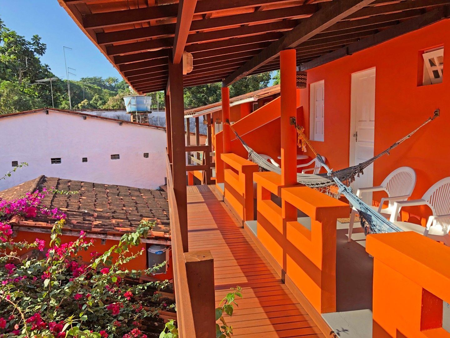 Interior de café com piso de madeira, mesas, cadeiras, área de bar e janelas com cortinas.