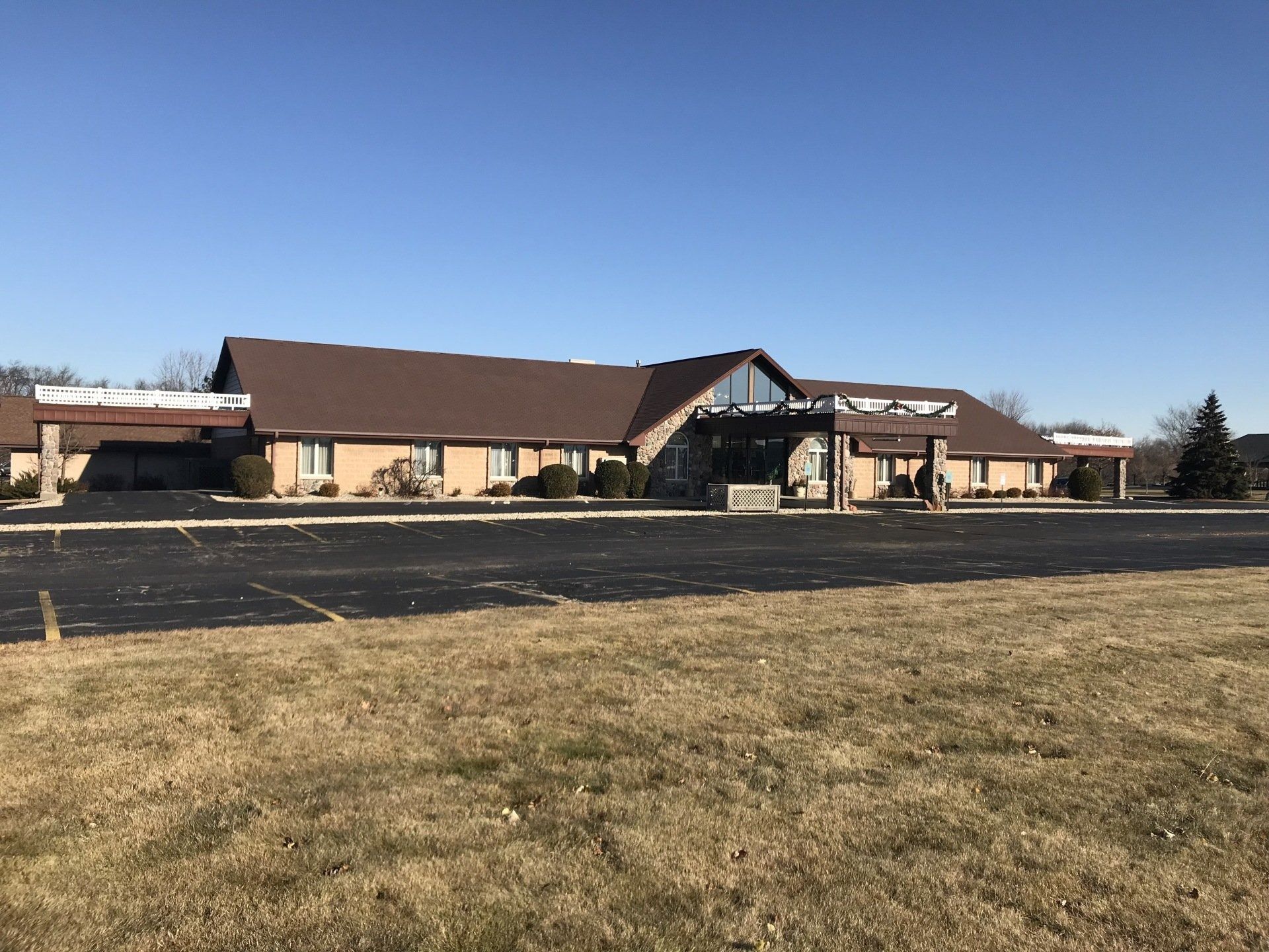 A one-story building with a brown roof and a large parking lot.