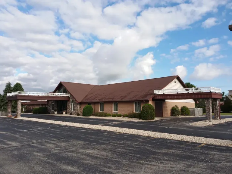 Brown-roofed brick building with a large parking lot, set against a blue sky, and dry grassy field in front.