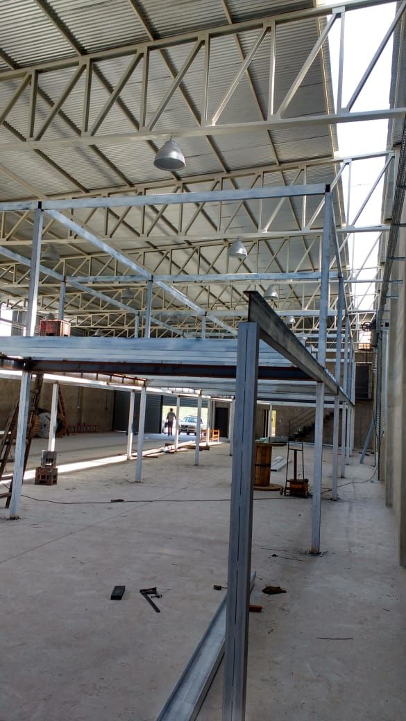 Obreros de la construcción con chalecos de seguridad en una obra de un edificio de vidrio con vigas de acero y andamios.