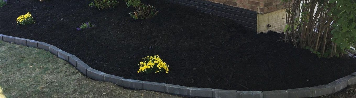 Curved stone border around a dark pond with yellow flowers and green plants along the edge