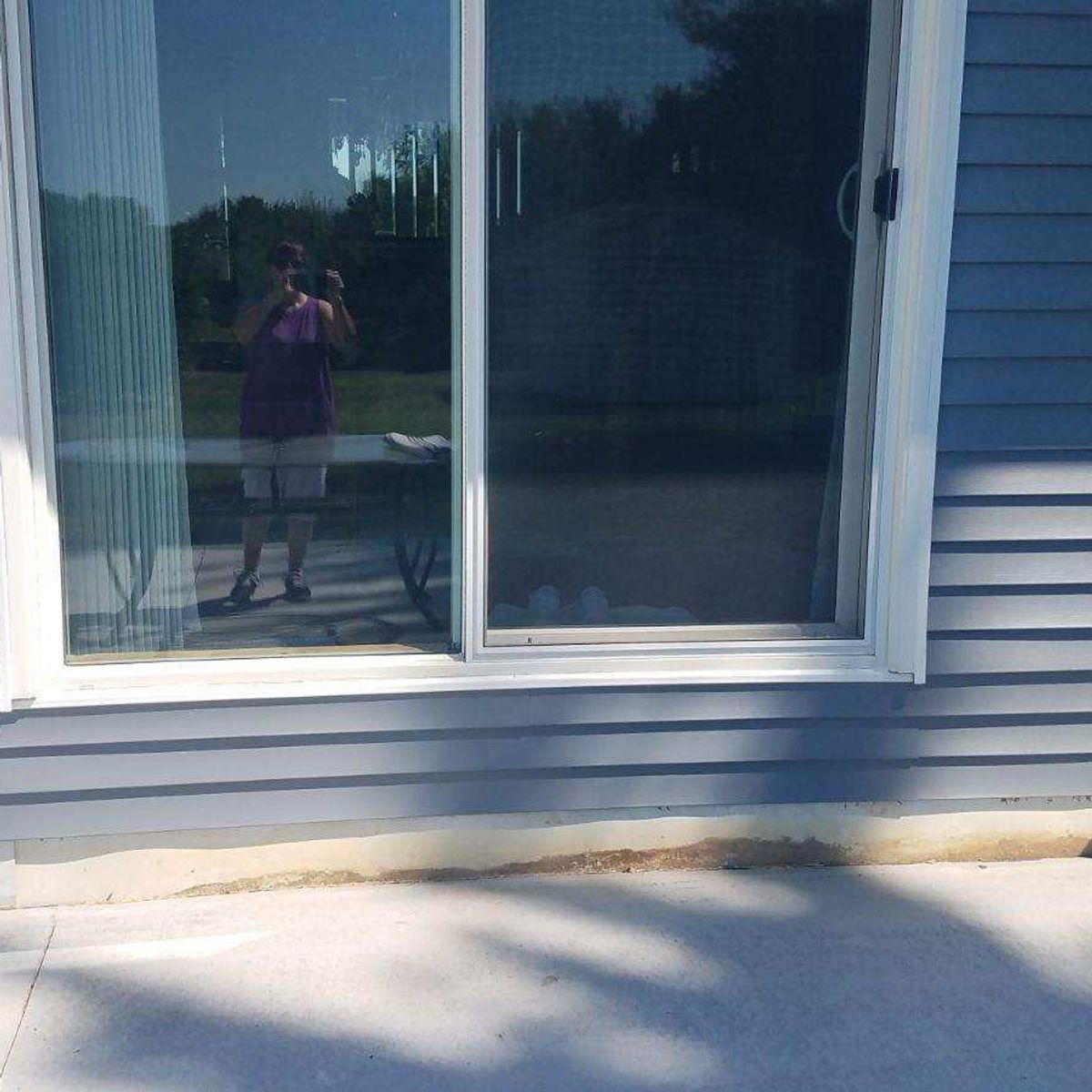Person reflected in a sliding glass door beside a house with blue siding and a concrete patio