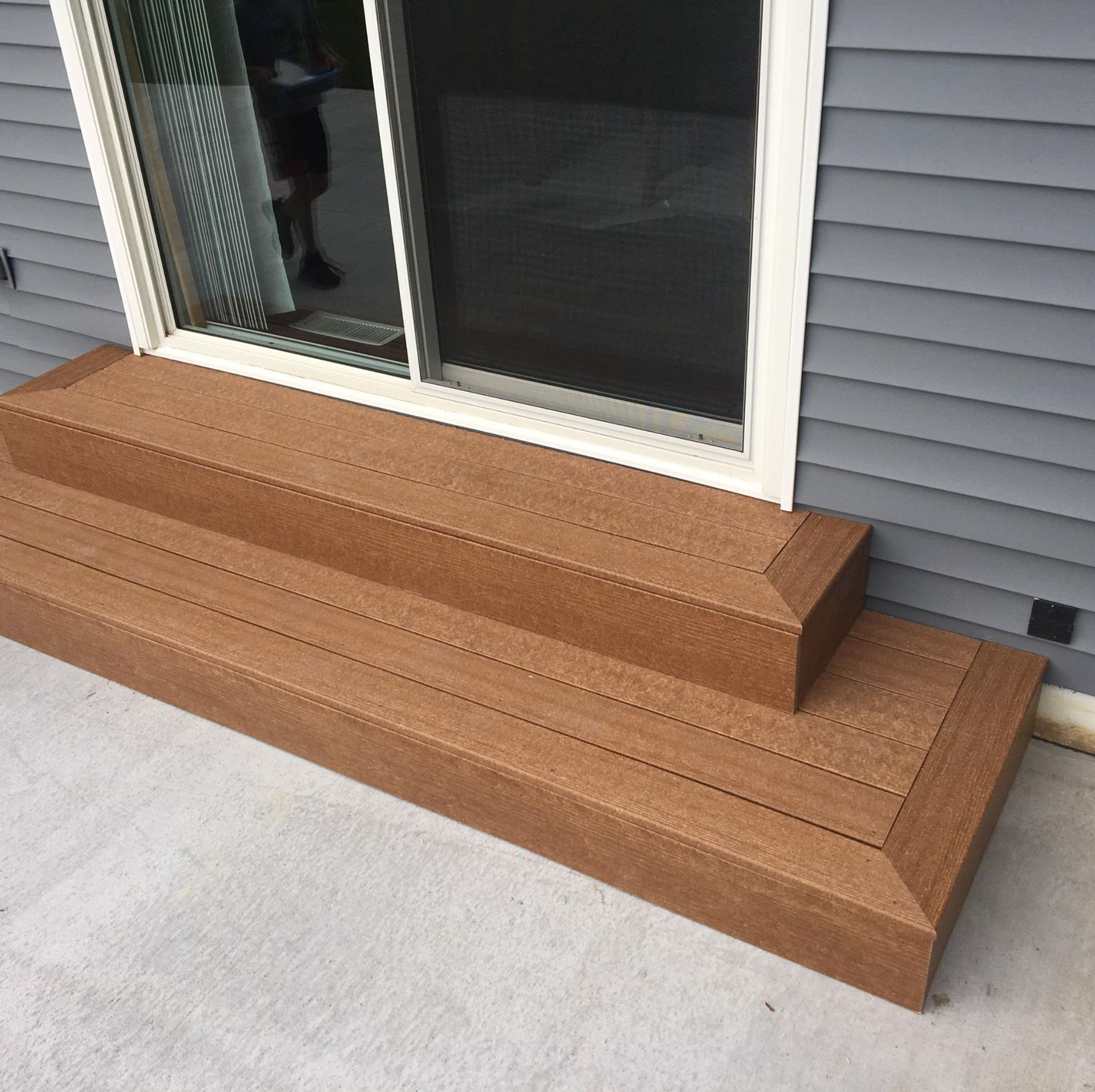 Brown wooden step platform under a sliding glass door on a concrete patio