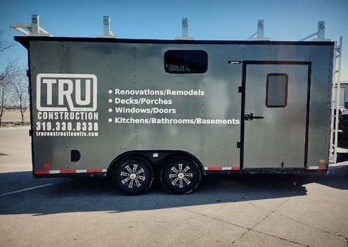 Black construction trailer with TRU logo and service list parked on a street.