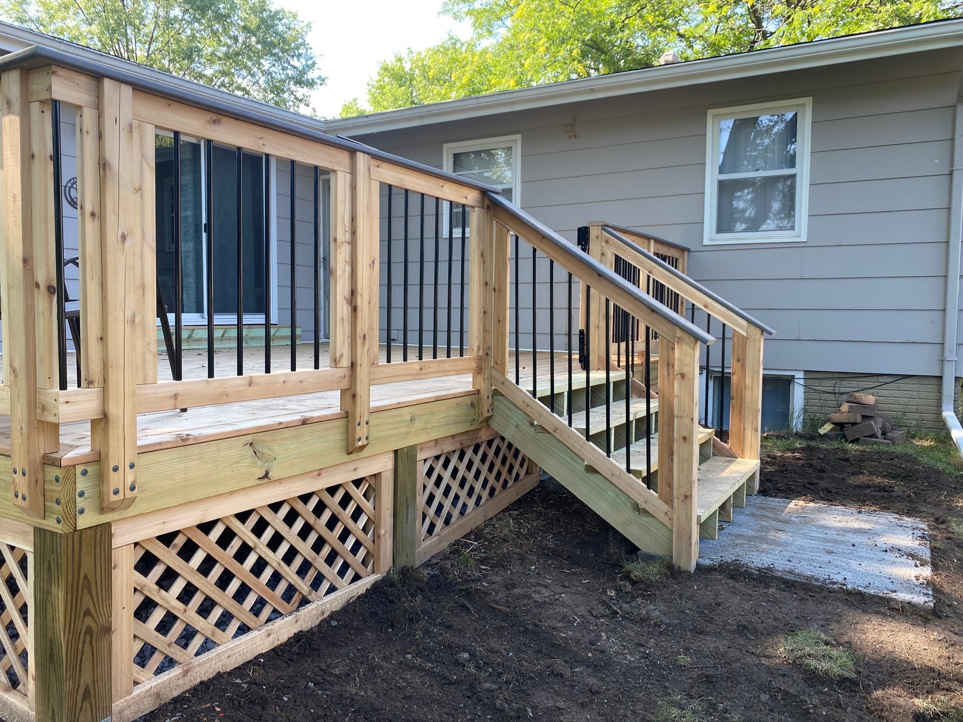 Wooden fence in a yard with green grass, trees, and glimpses of buildings.