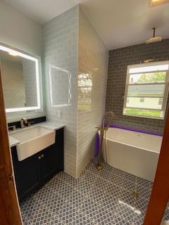 Modern bathroom with double sink, bathtub, large mirror, and patterned tile floor