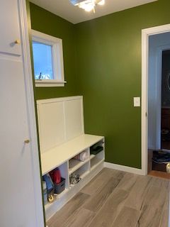 Green-walled entryway with white bench cubbies, a small window, and light wood floor.