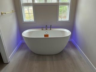 Modern bathroom with a freestanding white tub, window, and soft purple accent lighting