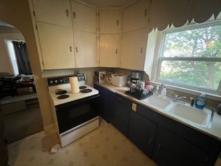 Small kitchen with cream cabinets, black lower cabinets, stove, sink, and a window over the counter.