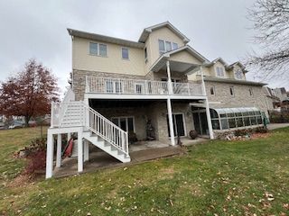 Large beige house with a white porch and stairs, viewed from a grassy yard on an overcast day