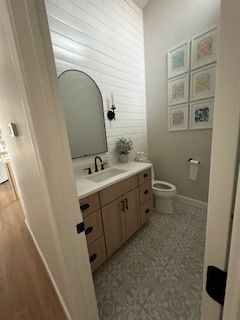 Small modern bathroom with white walls, wood vanity, round mirror, toilet, and patterned tile floor.