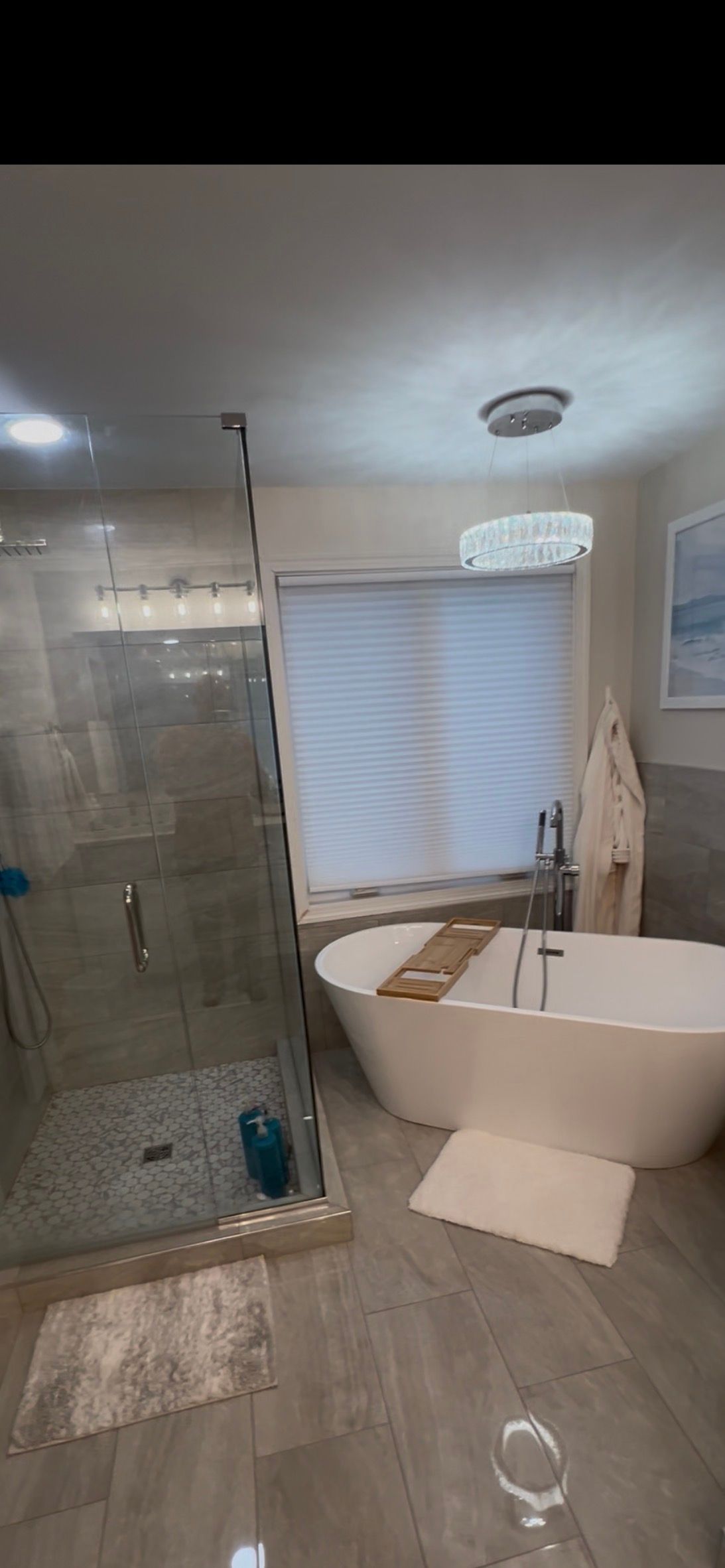 Modern bathroom with glass shower, freestanding tub, window blind, and light wood floor.