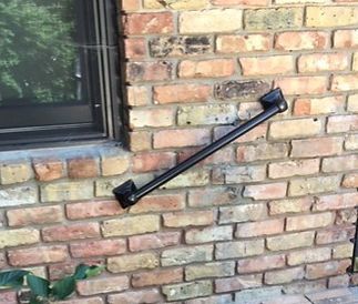 Black window crank handle mounted diagonally on a brick exterior wall beside a window