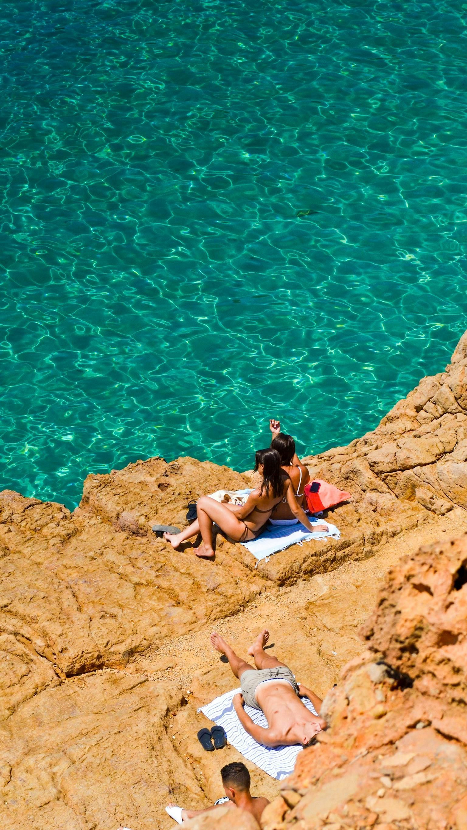 A group of people are sitting on the rocks near the ocean.