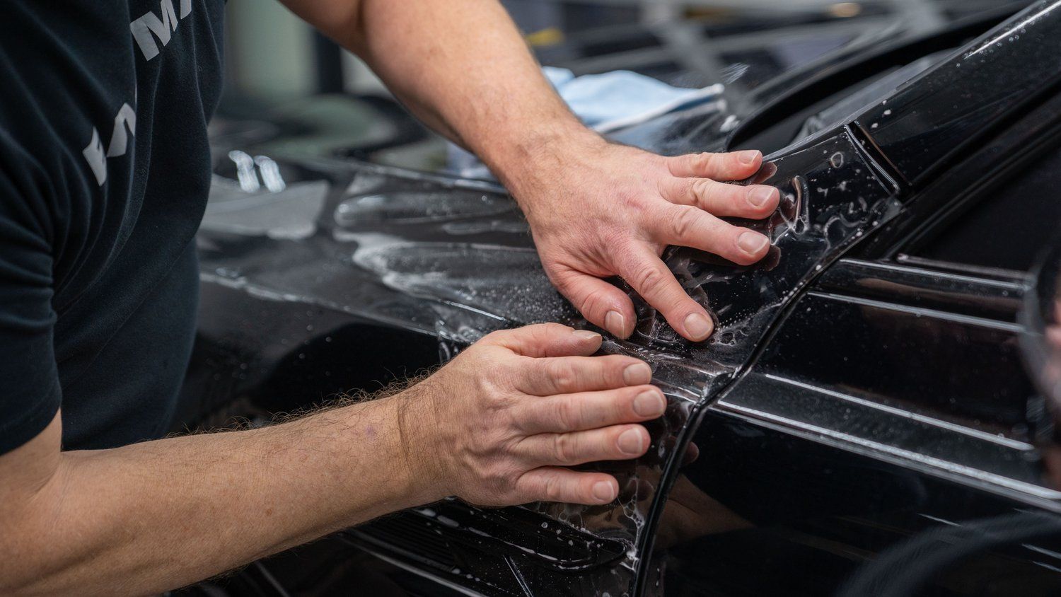 A man is wrapping a car with a clear plastic film.