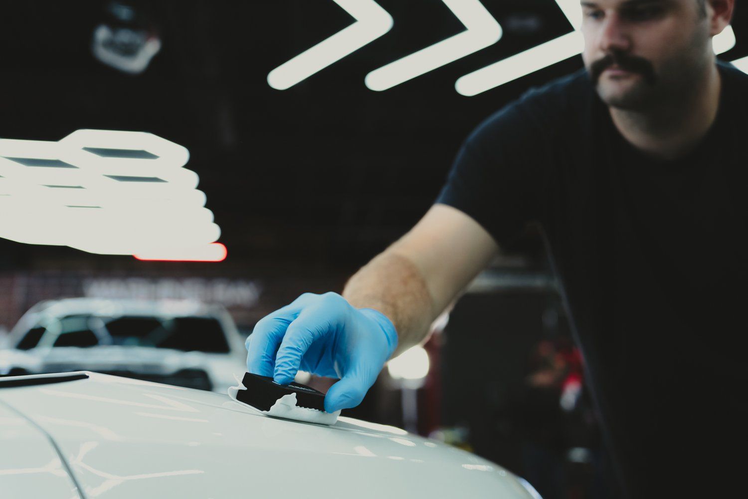 A man wearing blue gloves is polishing a white car.