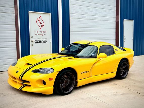 A yellow dodge viper is parked in front of a garage.