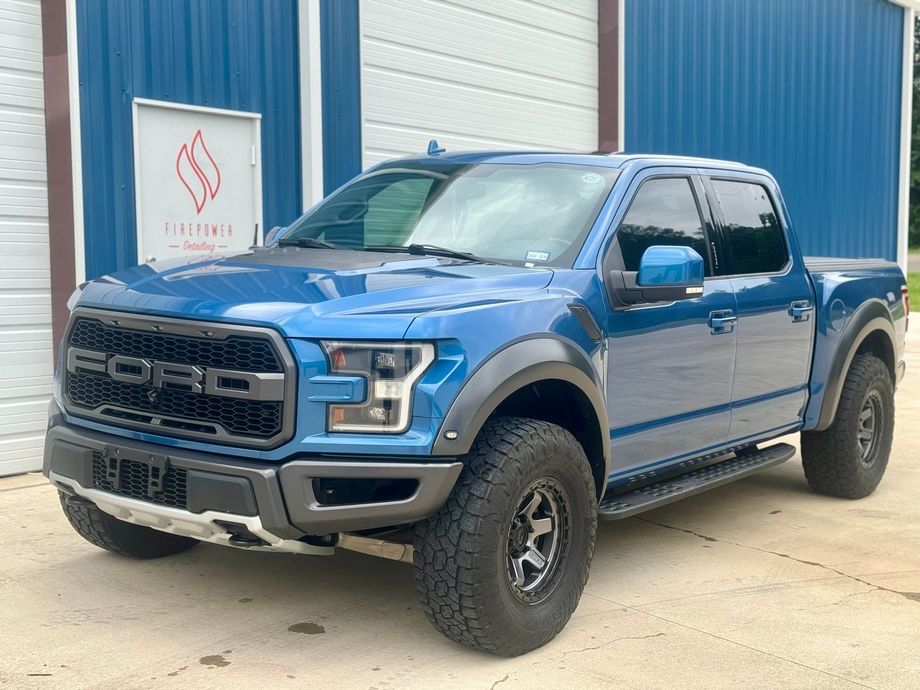 A blue ford raptor truck is parked in front of a blue building.