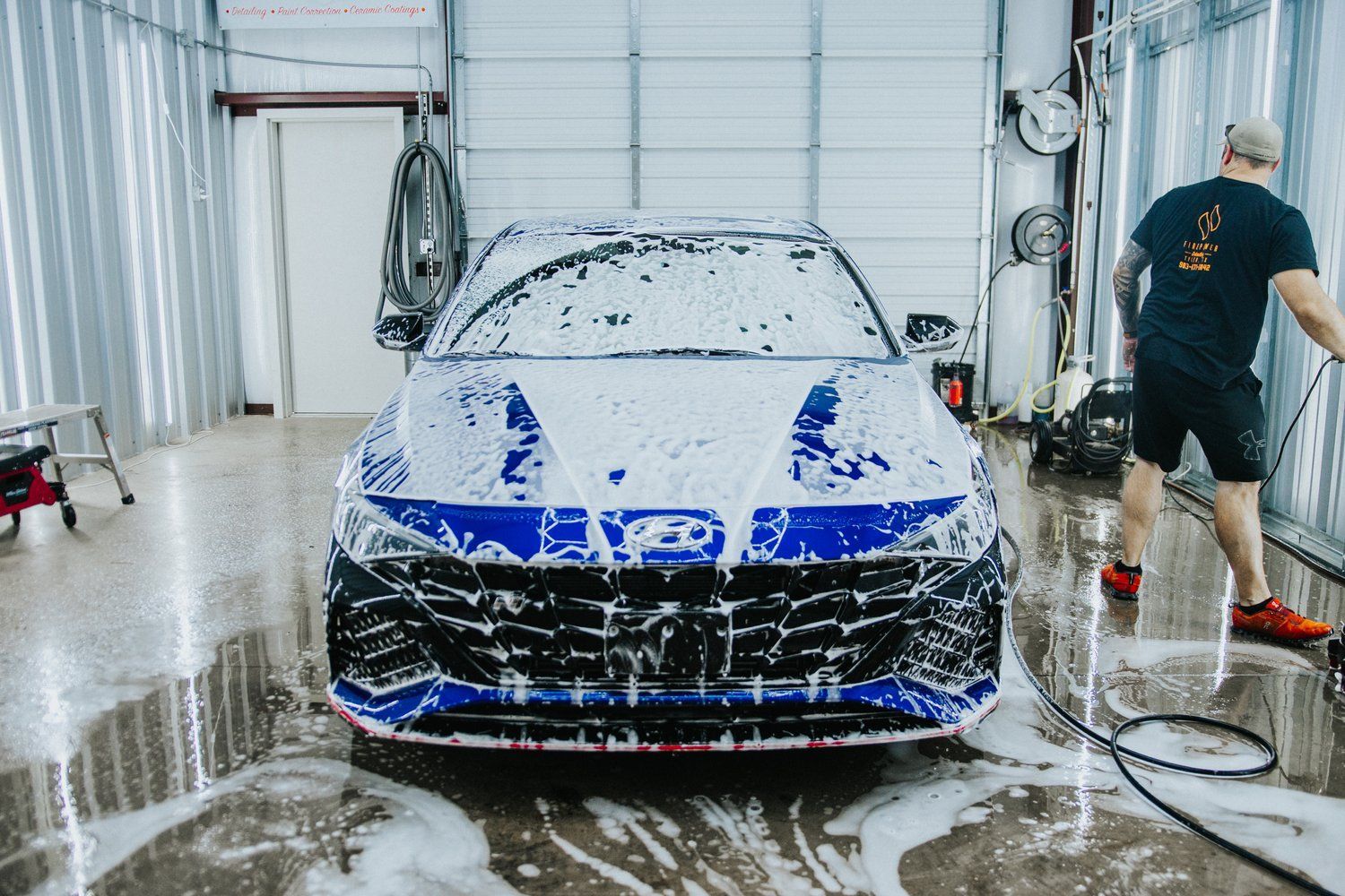 A man is washing a blue car with foam in a garage.