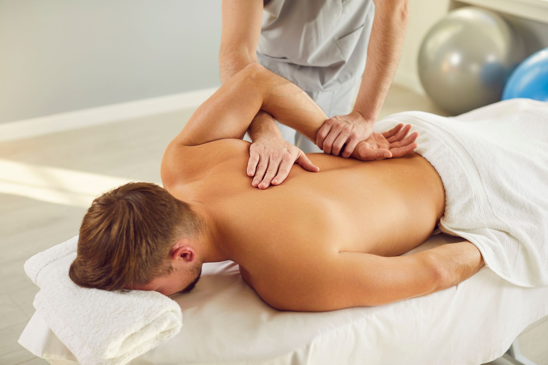Man receiving back massage, lying on a massage table. Therapist is pressing on his back with both hands.