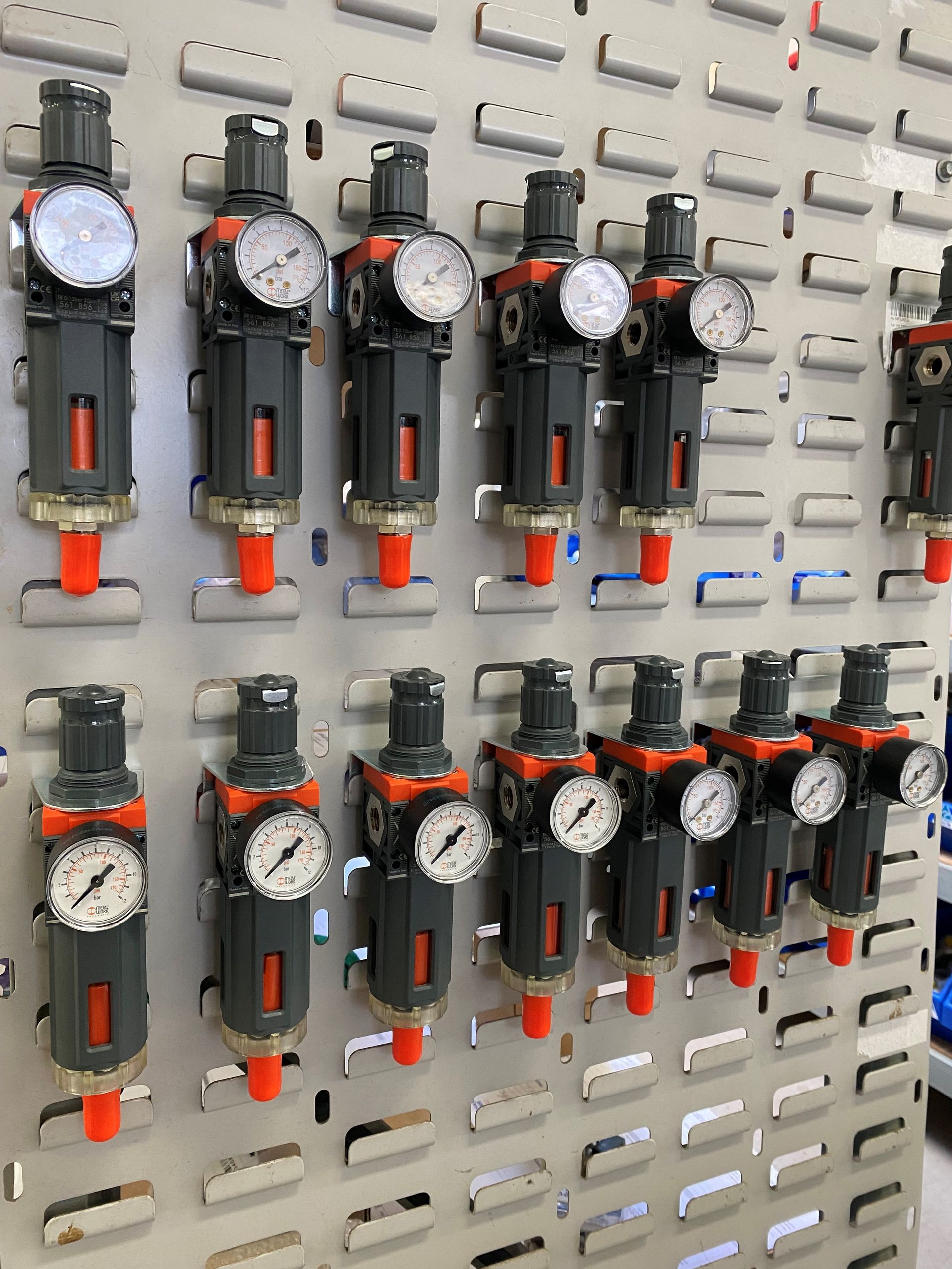 Rows of black pressure regulators with gauges and red valves mounted on a perforated panel.— Air & Lift Gear in Buderim, QLD