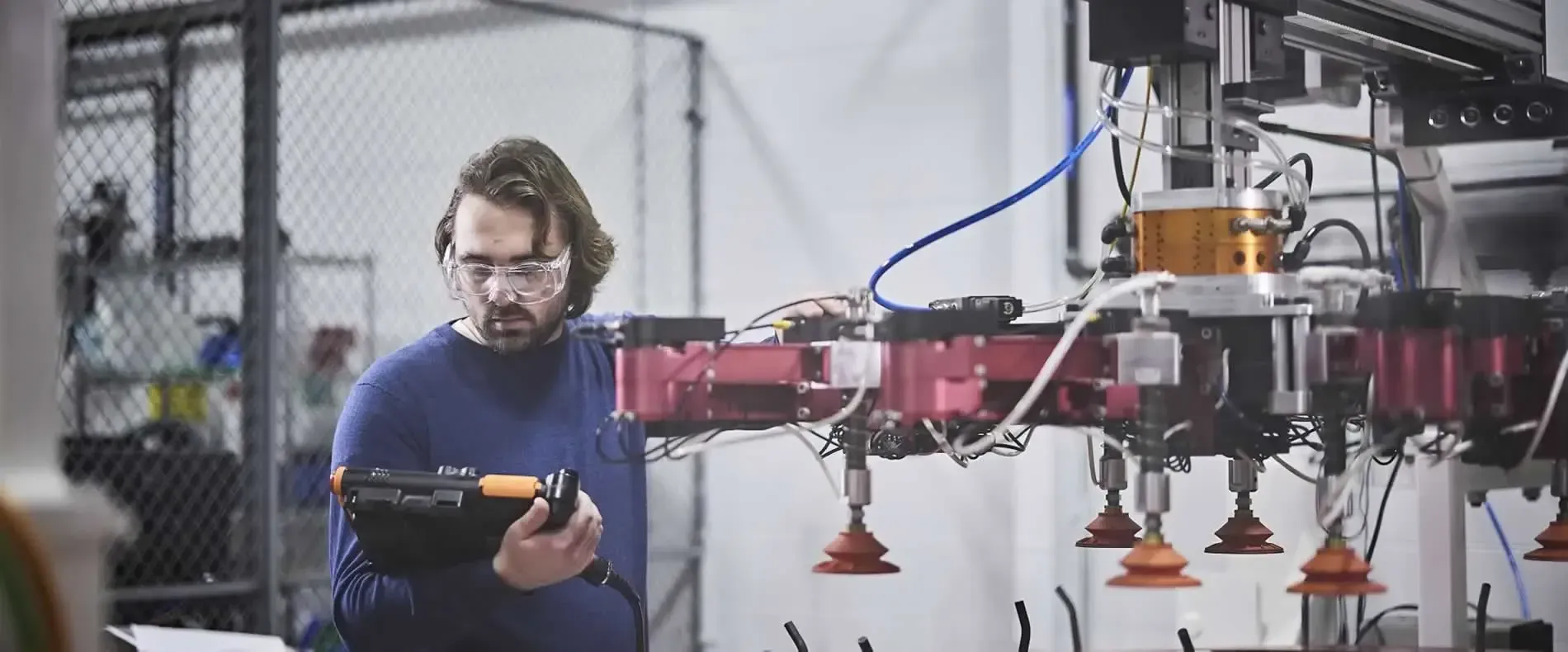Person inspecting a drone in a workshop, with red robotic arms and tools nearby— Air & Lift Gear in Buderim, QLD