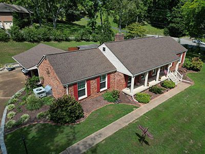 Aerial view of a brick house with red shutters, white porch columns, and a large green lawn.