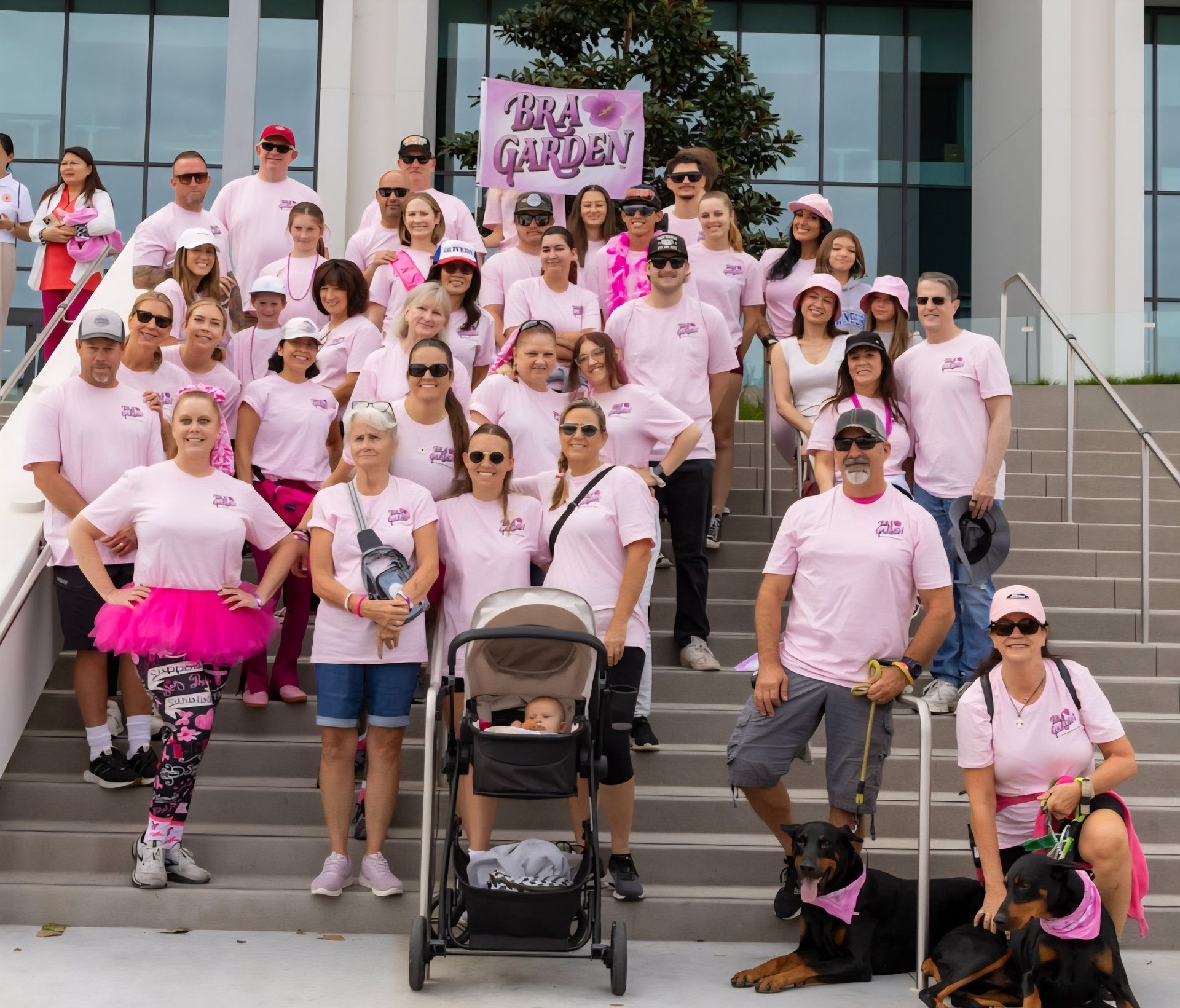 Group of people in pink shirts and accessories on steps, likely at a fundraising walk.