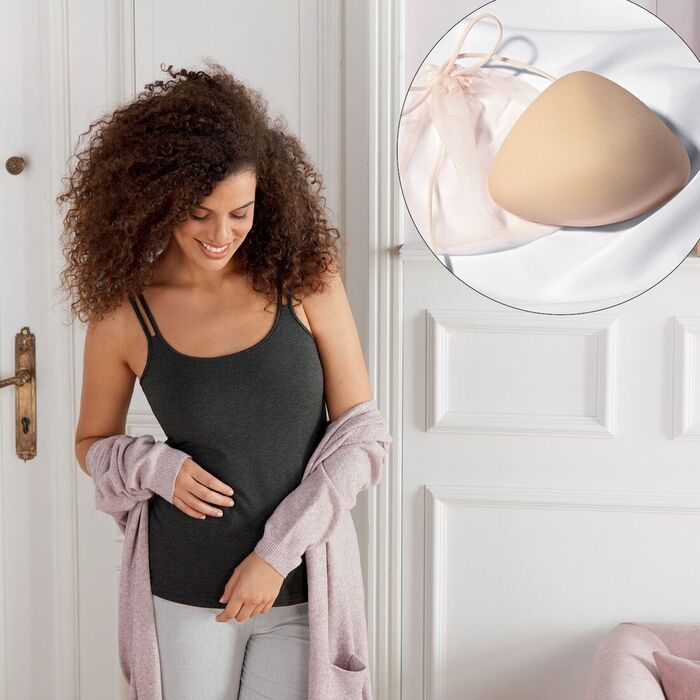 Woman in a black top with a pink cardigan, looking down, beside a bra cup insert close-up.
