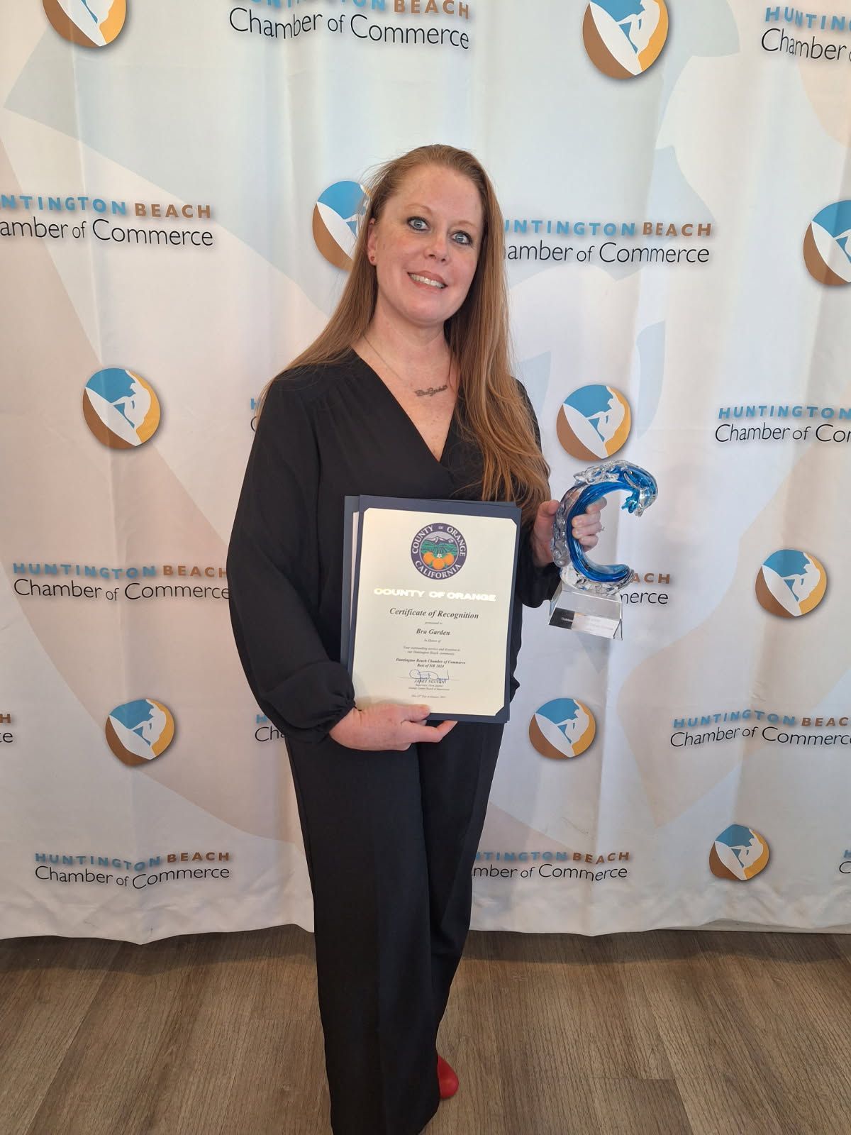Woman holding an award plaque and trophy at a Chamber of Commerce event backdrop