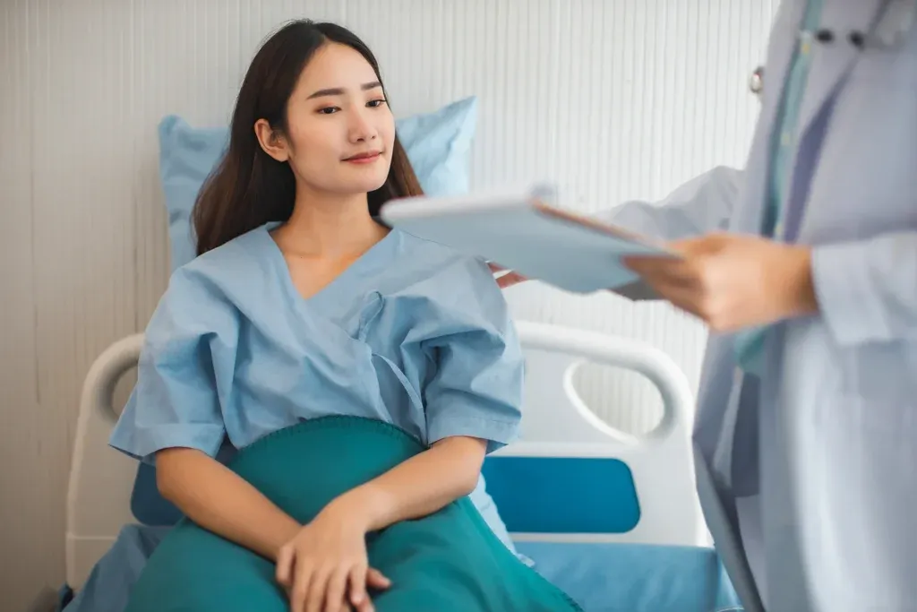 Patient seated on a hospital bed, listening to a doctor holding a clipboard