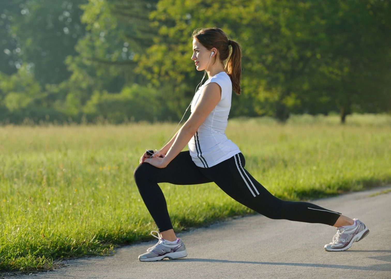 Woman stretching in a lunge on a path in a grassy park