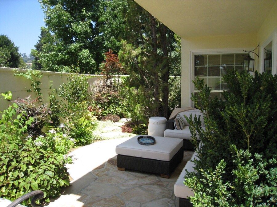 A patio with a couch and ottoman surrounded by trees and bushes
