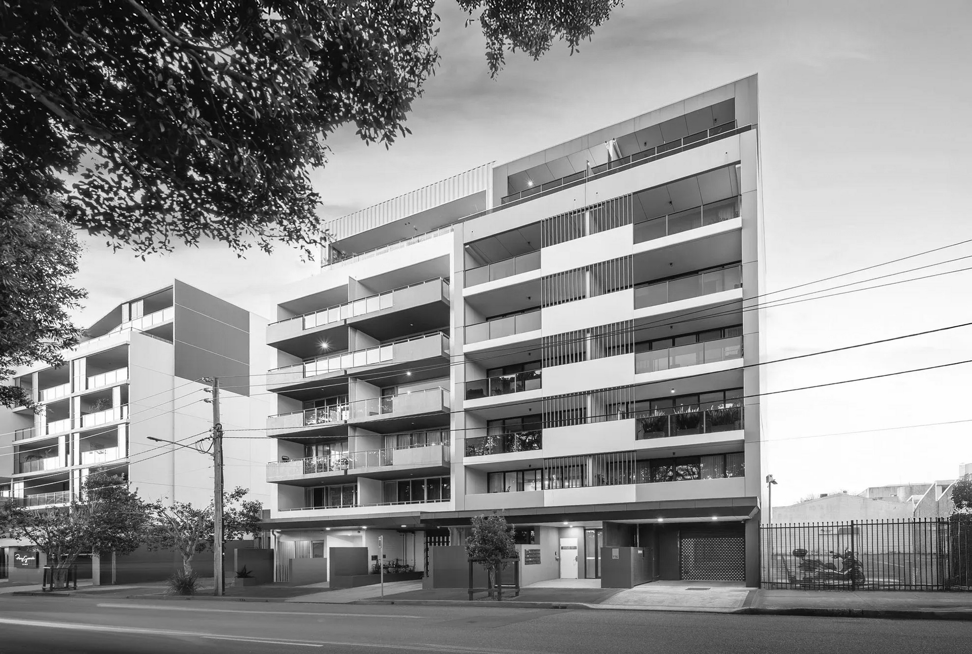 Black-and-white view of a modern apartment building with balconies and trees in front