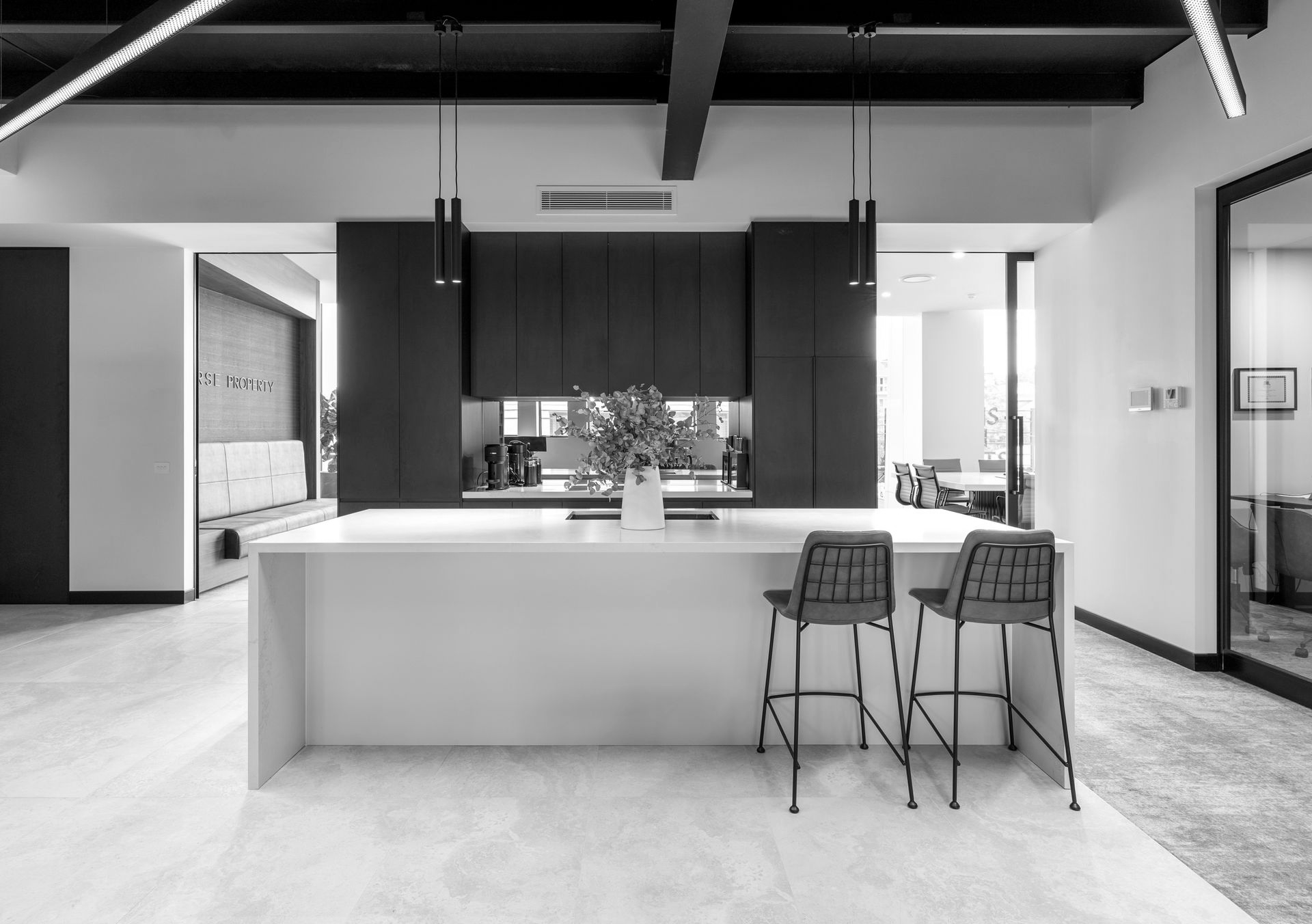 Modern kitchen with a large island, dark cabinets, and two bar stools in a bright open-plan room