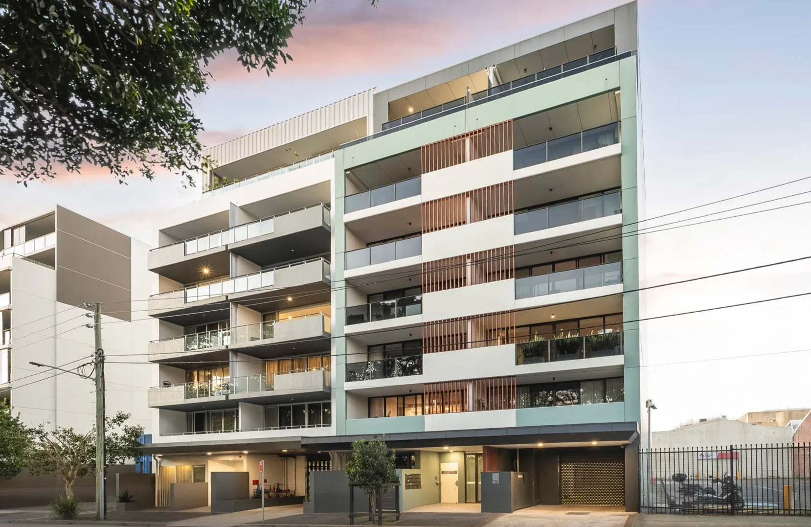 Modern apartment building with balconies and glass railings along a street at dusk