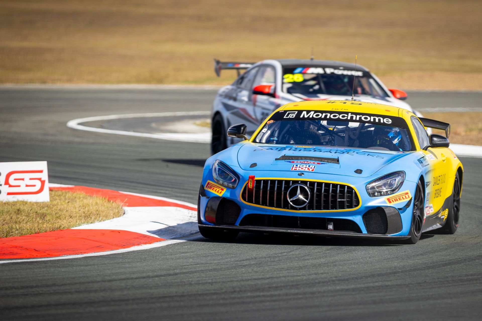 Two race cars on a track, blue Mercedes leading a silver car around a curve.