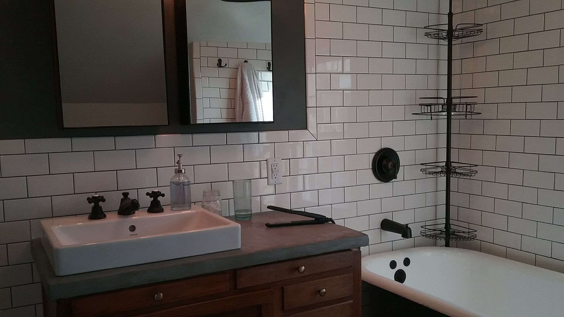 Bathroom with white tiled walls, dark cabinet, white sink, and black fixtures.
