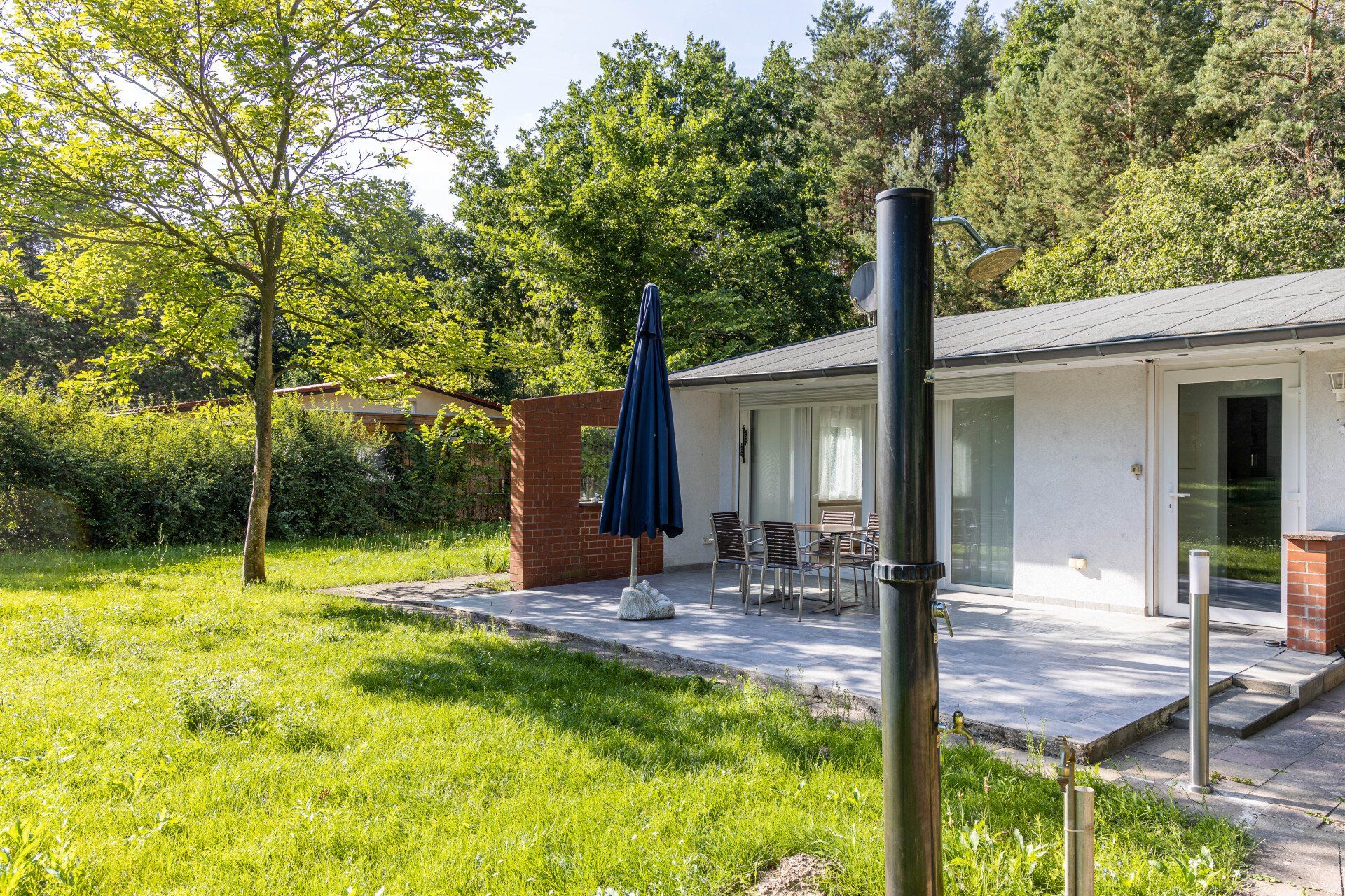 Ein Haus mit einer Terrasse und einem blauen Sonnenschirm davor.