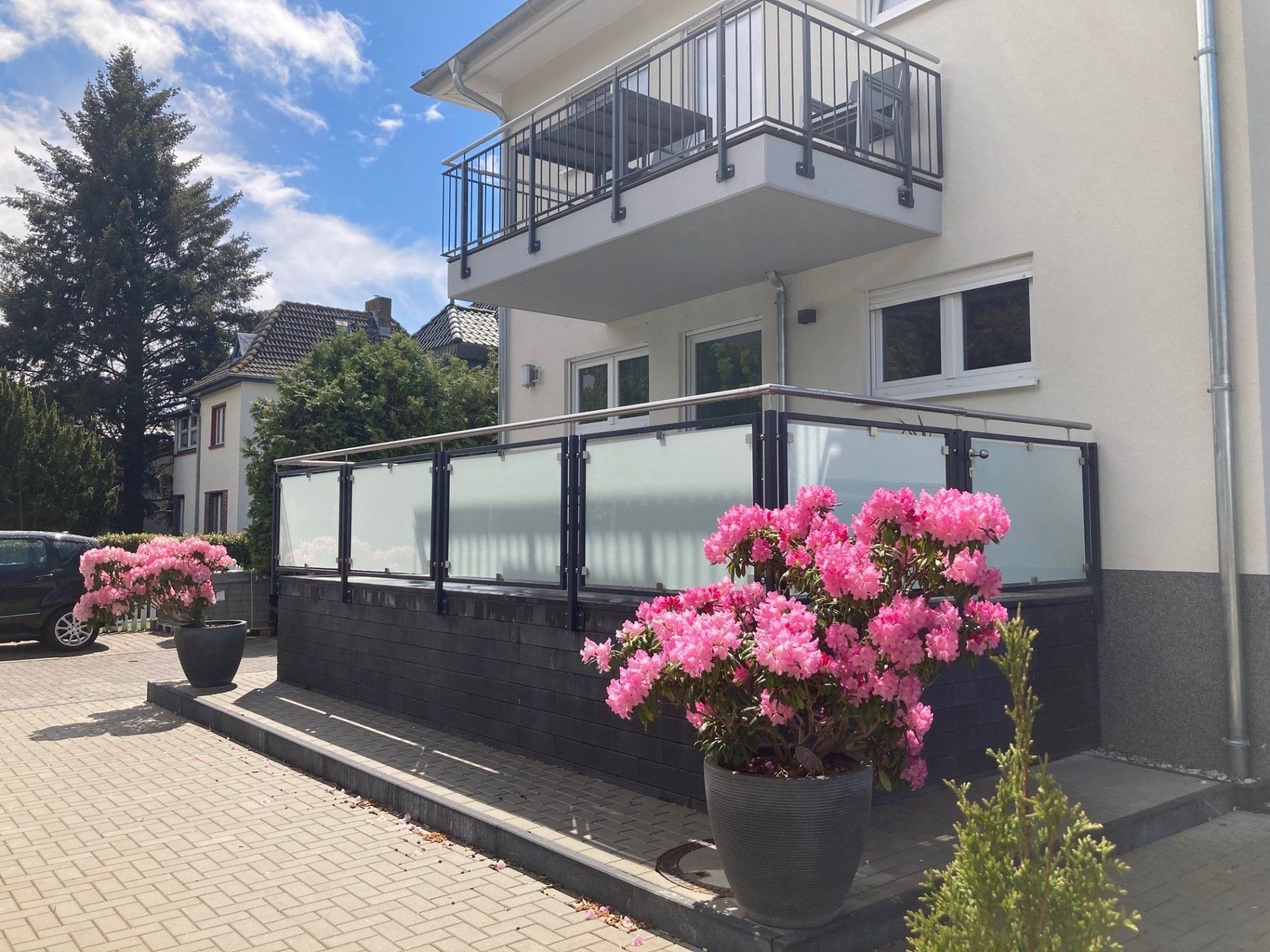 Ein weißes Haus mit einem Balkon und rosa Blumen davor