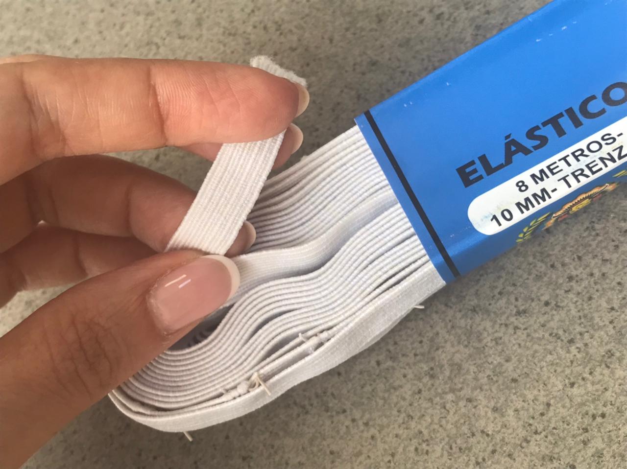 Hand holding a white elastic band from a blue package labeled “ELASTICO”